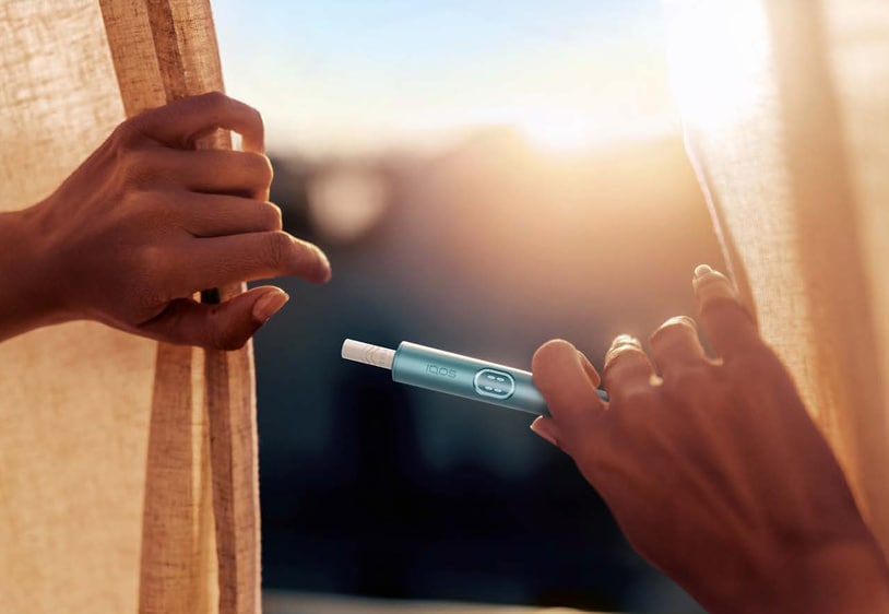 Close-up of a smoke-free tobacco device held by a person near a sunlit window