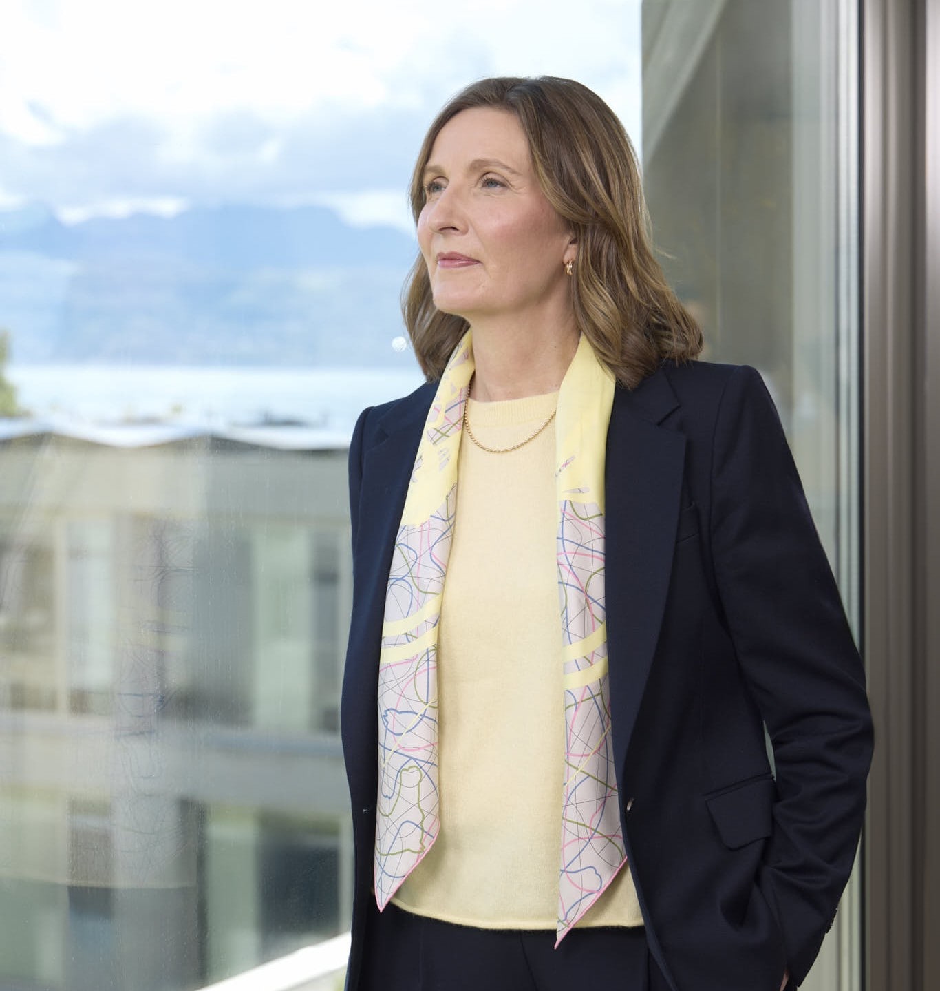 Moira Gilchrist standing beside a window with an urban landscape in the background.