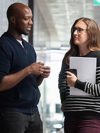 A smiling man and a woman holding a phone and paperwork, in an office.