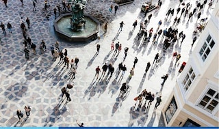 An ariel view of a crowd of people in a town square, with a fountain in the middle.