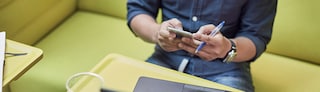 Man holding a phone while sitting at a laptop