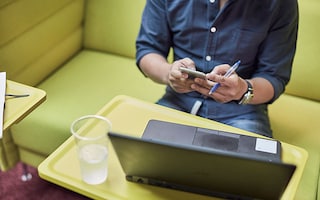 Man holding a phone while sitting at a laptop