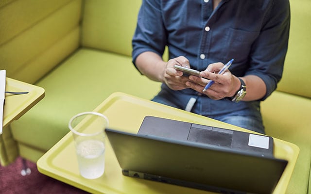 Man using his mobile phone while sitting by a laptop