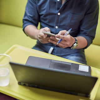 Man using his mobile phone while sitting by a laptop