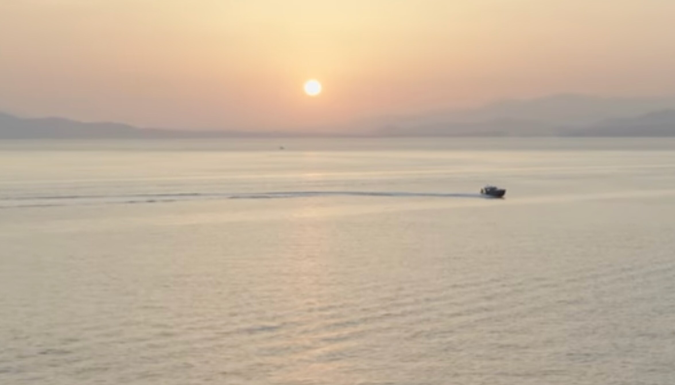 A speedboat on calm water in front of the sun on the horizon