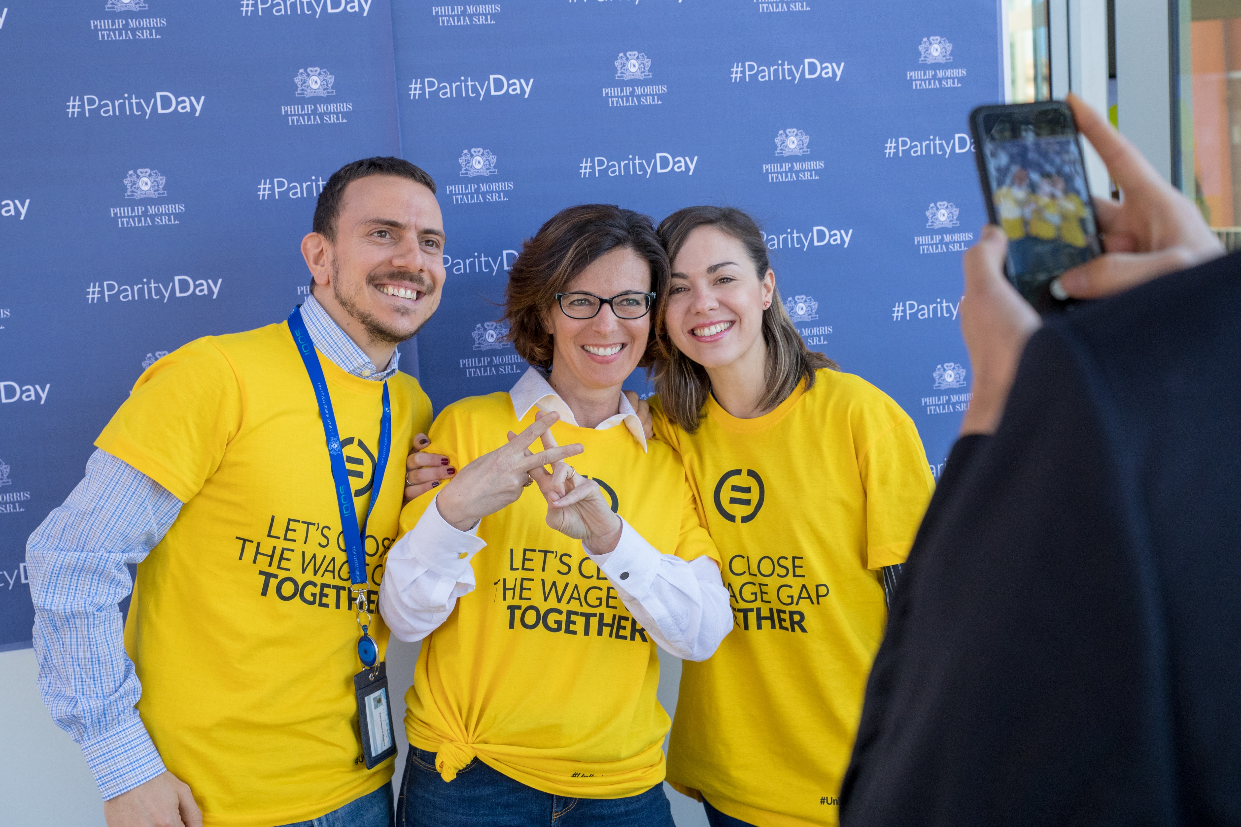 Two women and a man wearing yellow T-shirts to promote gender pay parity targets.