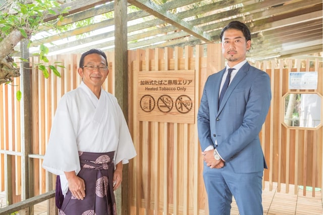 Two men standing in front of a no-smoking sign at the Qingdao Shrine, Japan.