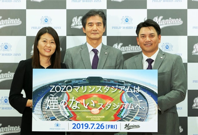 Two men and a woman holding a sign showing that ZOZO Marine Stadium is smoke-free, with text in Japanese.