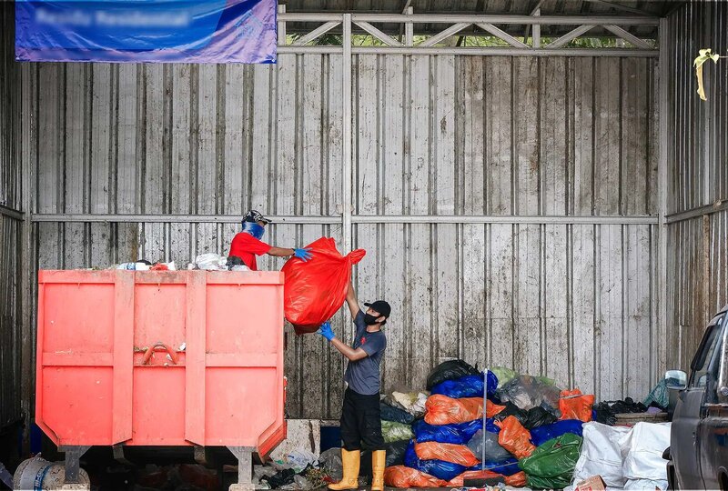 Two refuse workers clearing garbage bags from a skip.