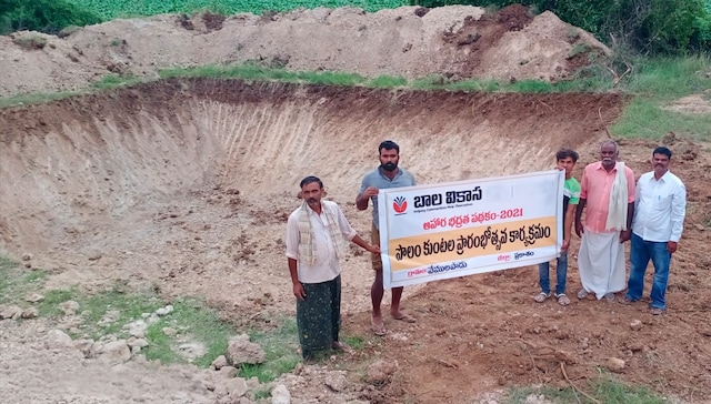PMI and NGO staff and farmers in front of a farm pond in India with a digger in the background