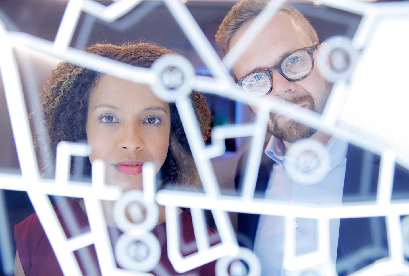 A man and a woman looking through a sculptural pattern of LED lights.
