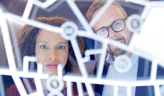 A man and a woman looking through a sculptural pattern of LED lights.