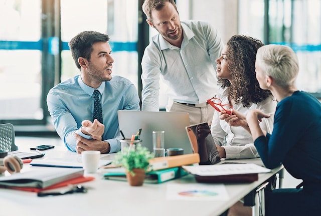 Four people having a meeting in an office, with laptops on the desk.