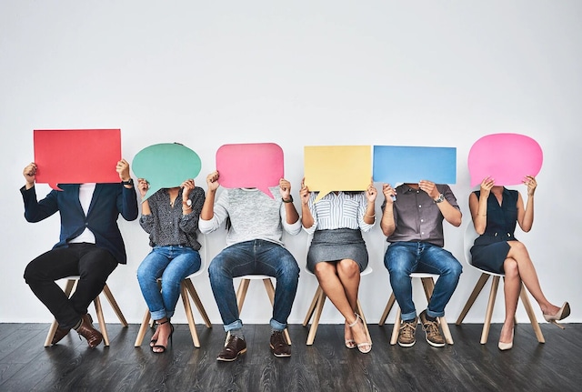 A row of seated people holding blank speech bubbles in front of their faces.