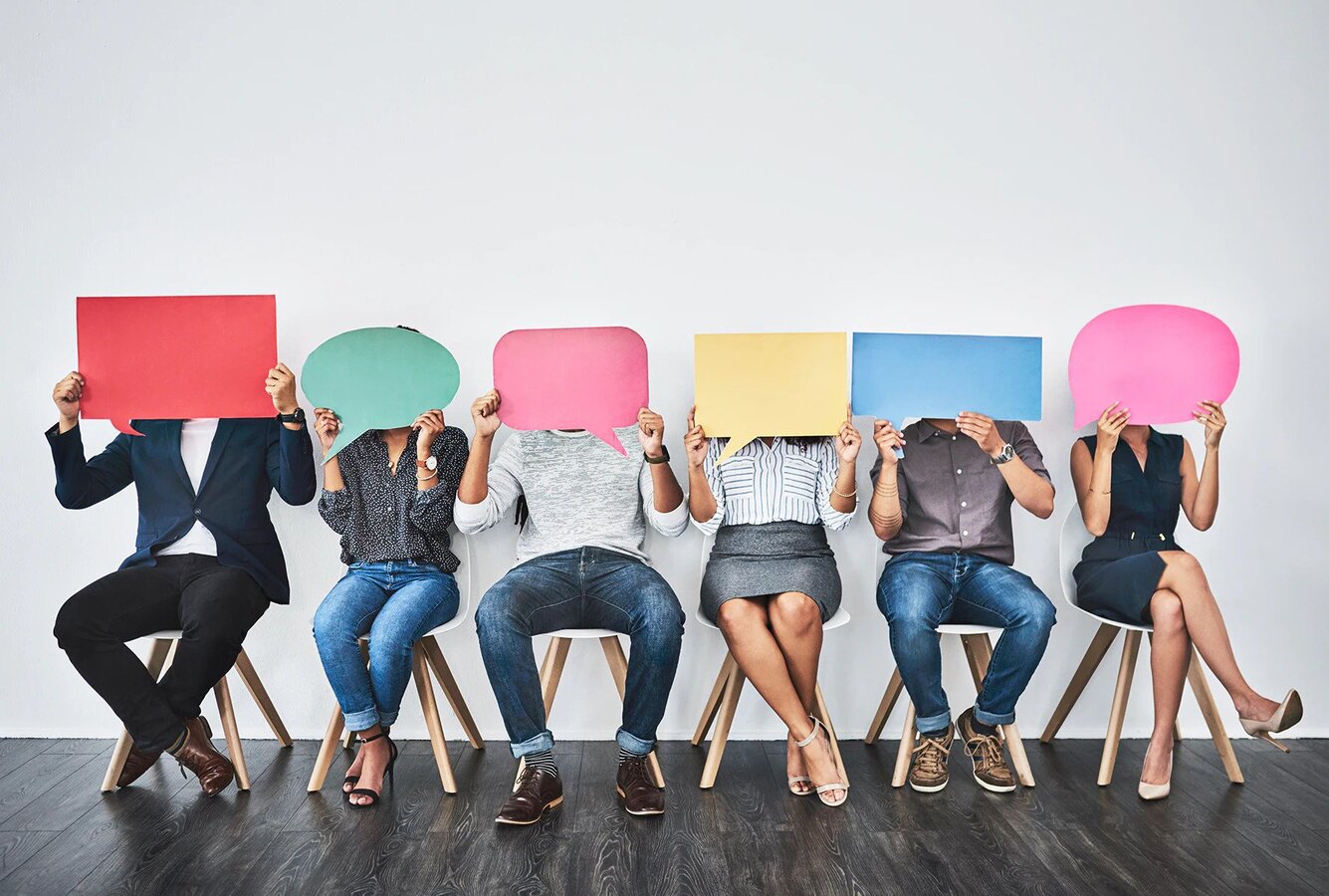 A row of seated people holding blank speech bubbles in front of their faces.