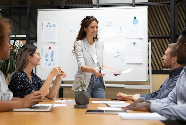 A smiling woman giving a presentation in front of a whiteboard.