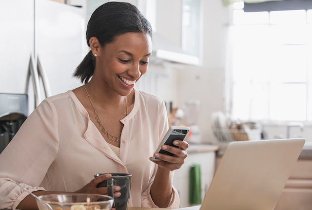 Woman sat in kitchen working smiling at phone