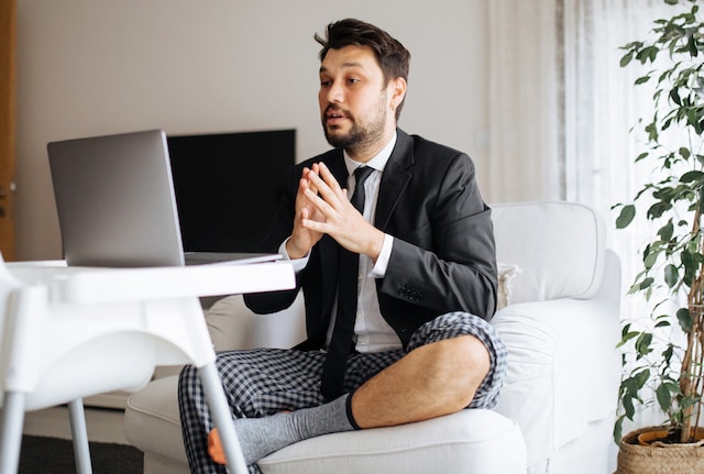 A man wearing a suit and pyjamas working from his sofa