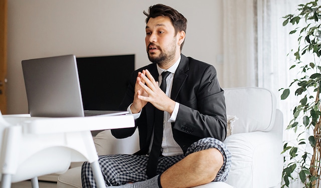A man wearing a suit and pyjamas working from his sofa